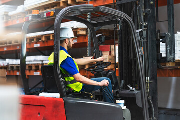 Caucasian male in a uniform and helmet driving the forklift through a storage room in a factory © Jesica