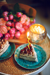 macro photo of the slice of a birthday cake with a single burning candle bokeh effect of a bouquet of flowers on the background