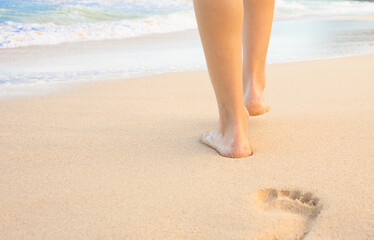 Beach travel - woman walking on sand beach leaving footprints in the sand. 