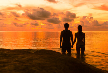 Man and woman standing together holding hand looking at a beautiful sunset. 