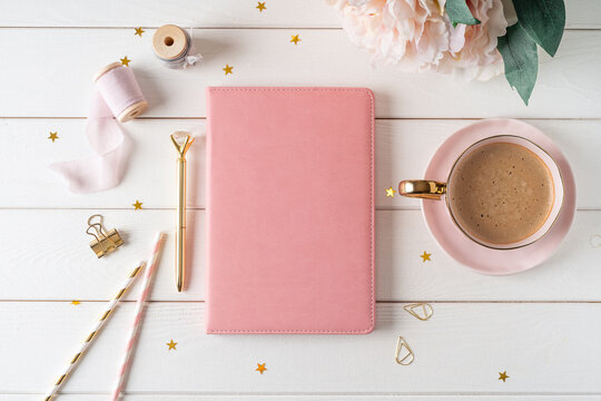 Top view of white working table background with blank paper notebook, cup of coffee. Flat lay peonies flowers, golden paper binder clips. Notepad and pen. Desktop mockup, workspace, stationery.