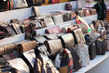 Showcase with fake handbags of famous brands. Variety of female bags at the market store.