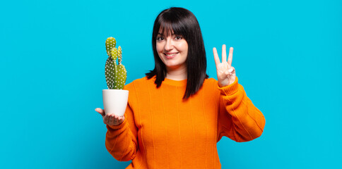 plus size pretty woman smiling and looking friendly, showing number three or third with hand...