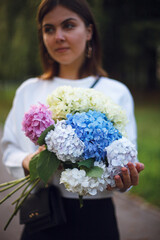 bouquet of white blue pink and yellow hydrangea in the hands of a girl on a blurred background