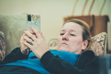 a middle-aged woman is lying in bed reading messages on a cell phone