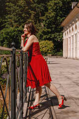 Obraz na płótnie Canvas Beautiful girl in red dress posing near the white house. Portrait of beautiful young brunette muse woman. Portrait of pretty girl on the street of town. Walk in downtown.
