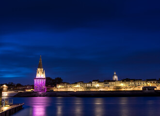 Fototapeta na wymiar Panoramic view of the old harbor of La Rochelle with its famous towers. night shot with pink lights for pink october. Pink October is breast cancer awareness month