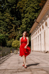 Beautiful girl in red dress posing near the white house. Portrait of beautiful young brunette muse woman. Portrait of pretty girl on the street of town. Walk in downtown.