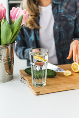 The girl prepares homemade lemonade with cucumber and lemon in the kitchen on a white table. Detox and diet food