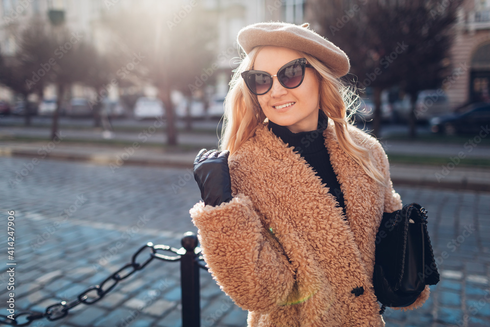 Wall mural Stylish woman wearing teddy coat beret sunglasses and holding purse outdoors. Spring fashionable female accessories.