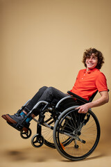 disabled man have fun sitting on wheelchair, smiling at camera, in action. isolated beige background