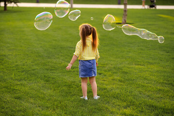 Happy little girl 4-5 years old plays with soap bubbles in the summer in the park. Children's lifestyle.