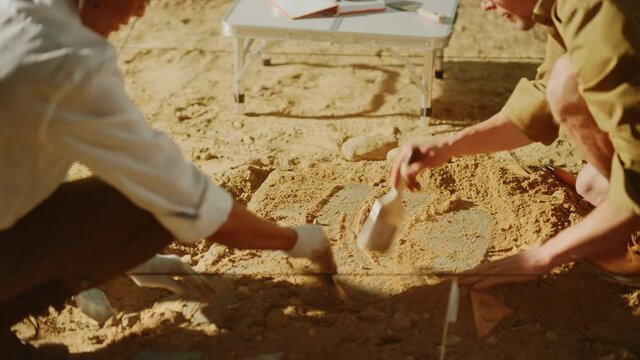 Archaeological Digging Site: Two Great Archeologists Work on Excavation Site, Carefully Cleaning, Lifting Newly Discovered Ancient Civilization Cultural Artifact, Historic Clay Tablet. Focus on Hands