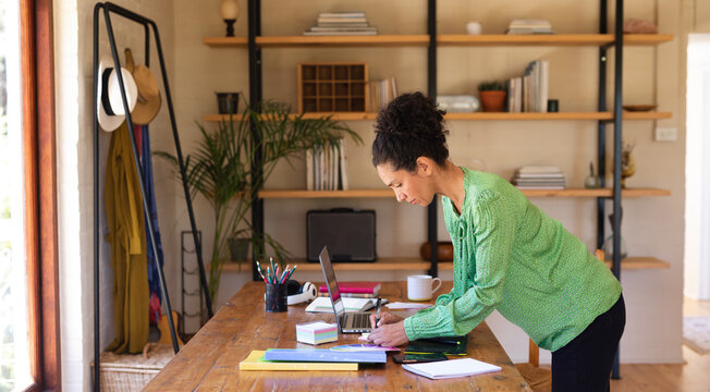 Caucasian woman writing, standing by desk, working from home