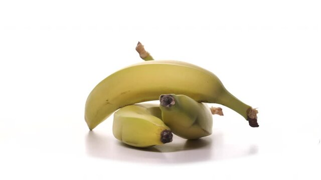 Three fresh yellow bananas are spinning on white background. Freshly picked plucked fruits on turntable, one banana on the other. Detailed view isolated.