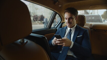 Happy male professional writing message on smartphone in business car.