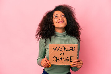 Young african american curly woman holding a we need a change cardboard dreaming of achieving goals and purposes