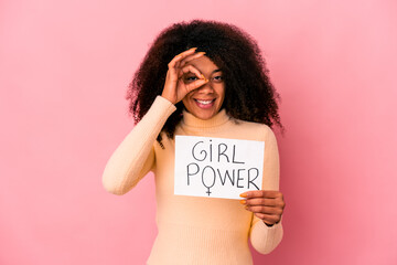 Young african american curly woman holding a girl power message on a placard excited keeping ok gesture on eye.