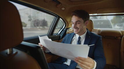 Smiling male professional rejoicing at good record in paperwork in business car.