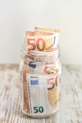 Fifty euro banknotes in a glass jar on rustic wooden table background with copy space. Savings concept.