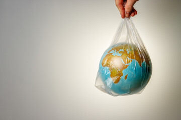The concept of World Environment Day. The man's hand holds the earth in a plastic bag. In the blank for social advertising there is a place for the inscription. - obrazy, fototapety, plakaty