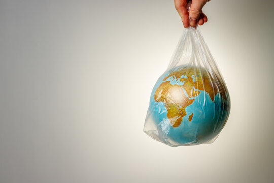 The Concept Of World Environment Day. The Man's Hand Holds The Earth In A Plastic Bag. In The Blank For Social Advertising There Is A Place For The Inscription.