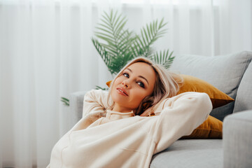 Relaxed serene pretty young woman, relax, calm dream sitting on the couch, enjoy wellbeing in cozy home modern living room   