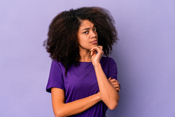 Young african american curly woman isolated on purple background suspicious, uncertain, examining you.