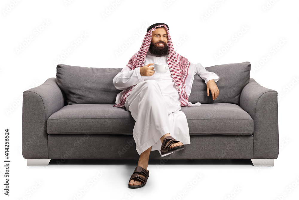 Poster saudi arab man sitting on a gray sofa and drinking a cup of tea