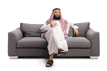 Saudi arab man sitting on a gray sofa and drinking a cup of tea
