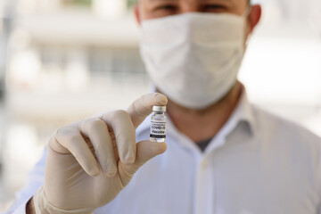 Doctor with white gloves holds bottle with COVID-19 vaccine. Concept of medicine, clinical trial and treatment due to SARS-CoV-2 coronavirus. Blur concept