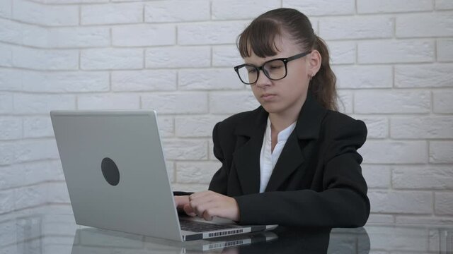 Teen work on computer in office. A view of a concentrated and dissatisfied little girl in the suit work on the computer.