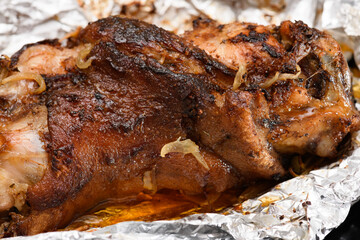 baked meat and fried onions on a baking sheet, pork ham on foil and wooden background, home cooking