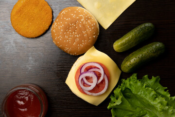 The process of making a burger from different ingredients. Top view. Tomatoes, onions, lettuce leaves, sauce, cutlet, cucumbers, cheese.