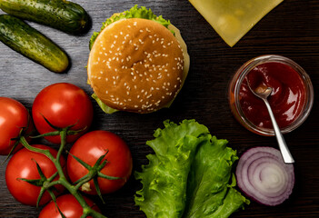 The process of making a burger from different ingredients. Top view. Tomatoes, onions, lettuce leaves, sauce, cutlet, cucumbers, cheese.