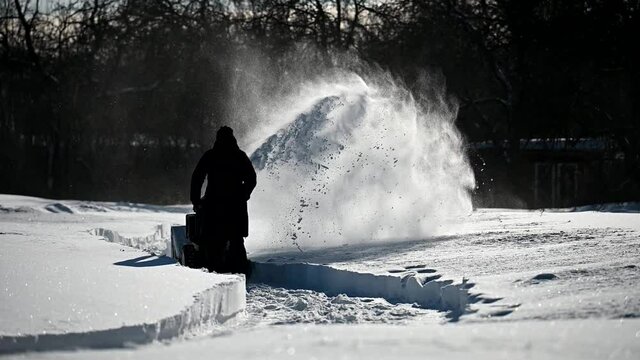 Slow motion footage of worker using snow blower at sunny day among snowdrifts