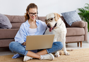 Cheerful woman and dog in glasses surfing laptop