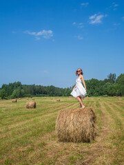 Naklejka na ściany i meble Girl dancing on a bale of hay on a summer day
