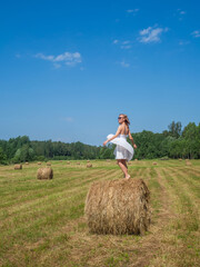 Naklejka na ściany i meble Girl dancing on a bale of hay on a summer day