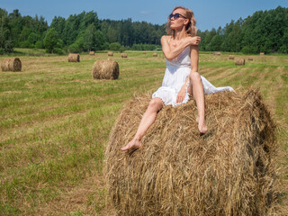 Naklejka na ściany i meble Girl in a field by a bale of hay on a summer day