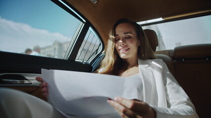Cheerful business woman analysing statistics in documents in automobile.