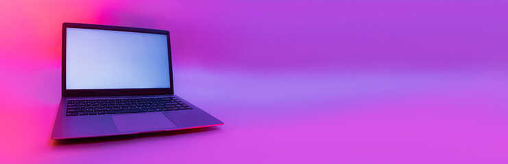 Slim modern laptop with white screen on the background creative light. Mockup in colorful bright neon UV blue and purple lights.