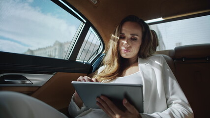 Tired business lady reading bad news on digital tablet in car. Rich woman in car