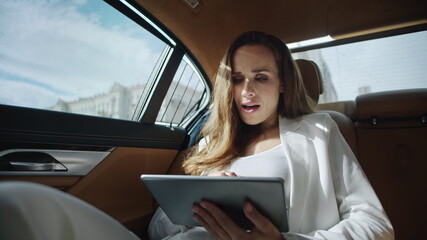 Surprised business woman reading good news on tablet computer in luxury car.