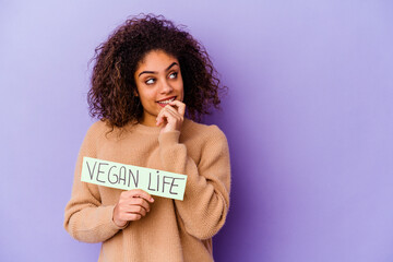 Young African American woman holding a Vegan life placard isolated relaxed thinking about something looking at a copy space.