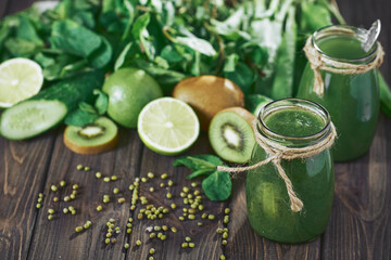 Blended green smoothie with ingredients on the stone board, wooden table selective focus