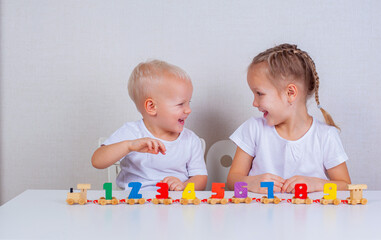 Children play a toy wooden train with numbers at the table and laugh.
