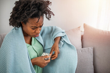 Sick woman with headache sitting under the blanket. Sick woman with seasonal infections, flu, allergy lying in bed. Sick woman covered with a blanket lying in bed with high fever and a flu, resting.