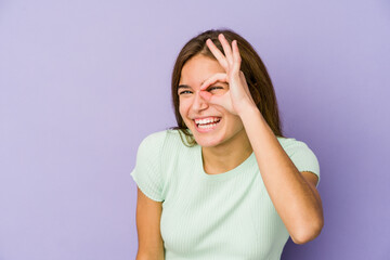 Young skinny caucasian girl teenager on purple background excited keeping ok gesture on eye.