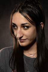 Fototapeta premium Joven modelo caucásica de pelo castaño oscuro, guapa, en fondo gris oscuro, mirando maliciosamente hacia un lado